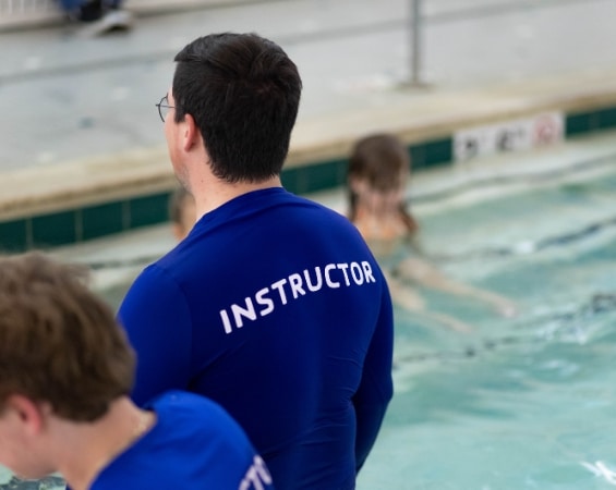 a man in a blue shirt with white text instructing swim school